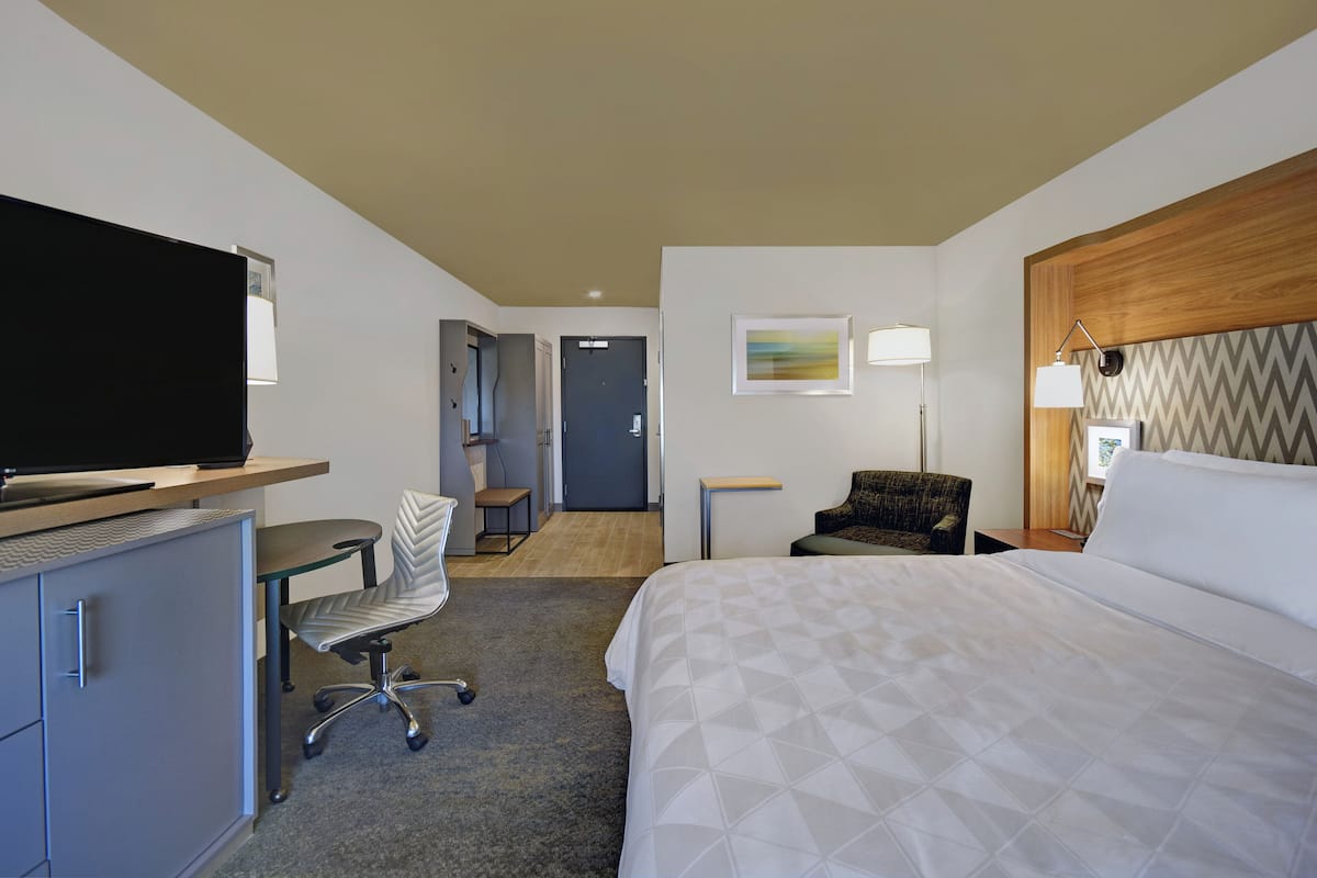Une chambre d’hôtel avec un lit, un bureau, une chaise, une télévision et un tableau au mur.