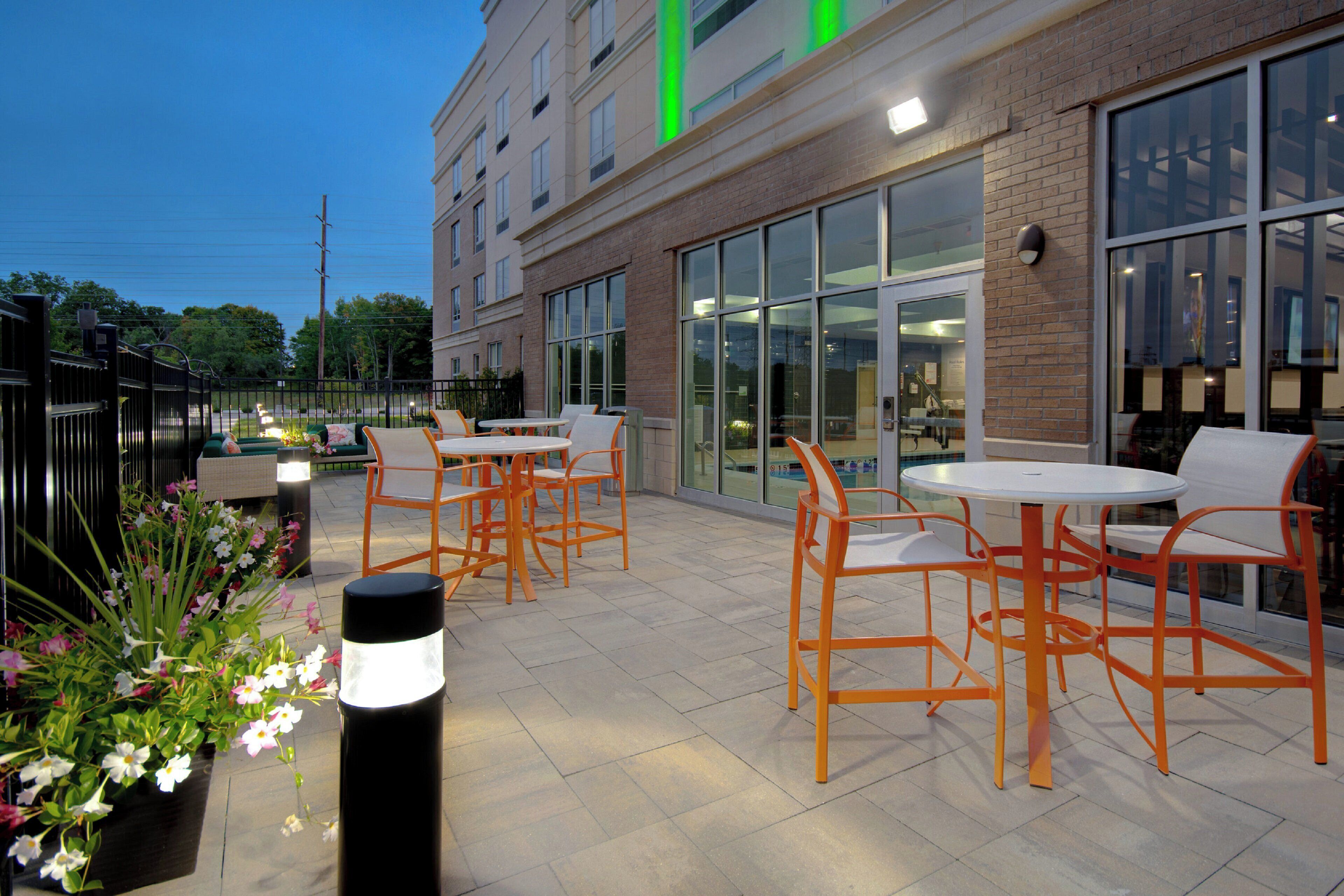 An outdoor patio area with tables and chairs, large windows, and a brick building facade.