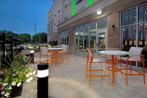 An outdoor patio area with tables and chairs, large windows, and a brick building facade. - Holiday Inn Grand Rapids North - Walker by IHG (Grand Rapids)