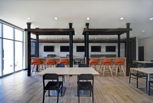 A modern conference room with wooden tables and chairs, large windows, and a high ceiling with recessed lighting.