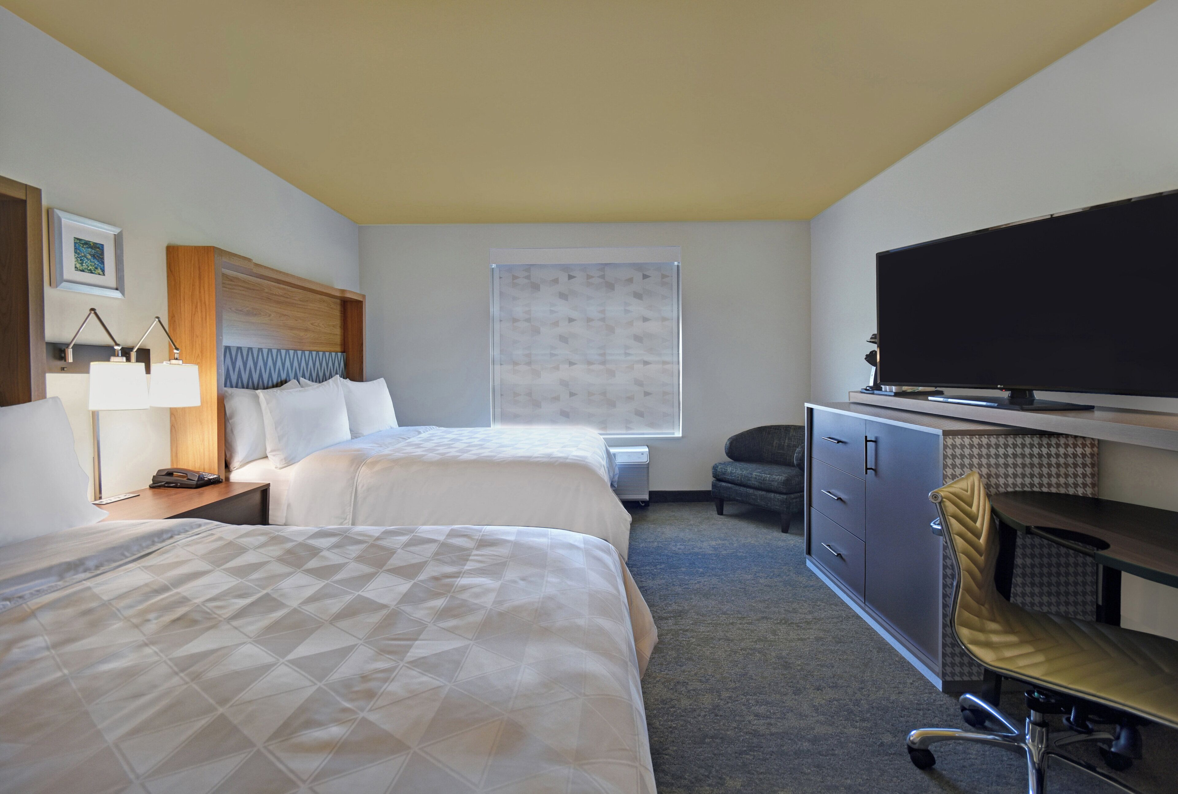 A hotel room with two beds, a desk, a television, and a chair.