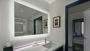 A modern bathroom with a large mirror, a sink, and a toilet visible through an open door. - Holiday Inn Grand Rapids North - Walker by IHG (Grand Rapids)