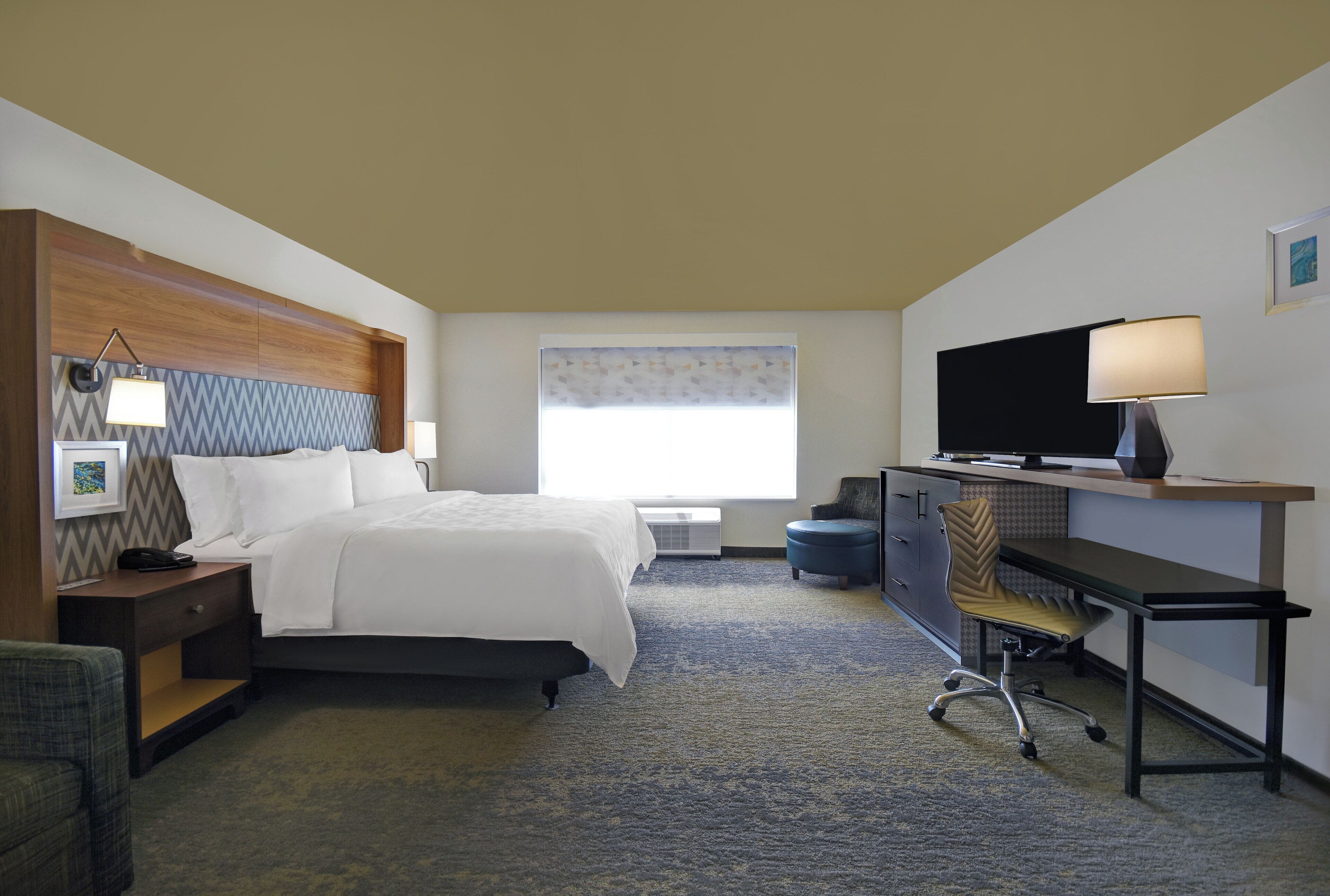Une chambre d’hôtel avec un lit, un bureau, une chaise, une télévision et une fenêtre.