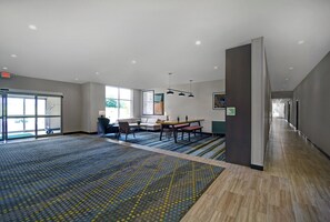 Une pièce spacieuse avec une grande fenêtre, un coin repas comprenant une table et des chaises, et un sol recouvert de moquette.