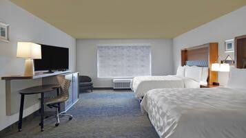 A hotel room with a desk, two beds, a television, and a window.