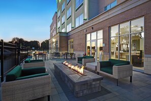 An outdoor seating area with fire pits and wicker furniture, adjacent to a building with large windows and a visible entrance. - Holiday Inn Grand Rapids North - Walker by IHG (Grand Rapids)