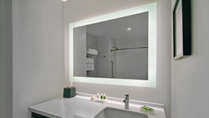 A modern bathroom with a white sink, a large mirror, and a shower visible in the reflection. - Holiday Inn Grand Rapids North - Walker by IHG (Grand Rapids)