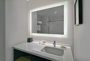 A modern bathroom with a white sink, a large mirror, and a shower visible in the reflection. - Holiday Inn Grand Rapids North - Walker by IHG (Grand Rapids)