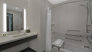 A modern bathroom with a large mirror, a sink, a shower with a glass door, and a small towel rack. - Holiday Inn Grand Rapids North - Walker by IHG (Grand Rapids)