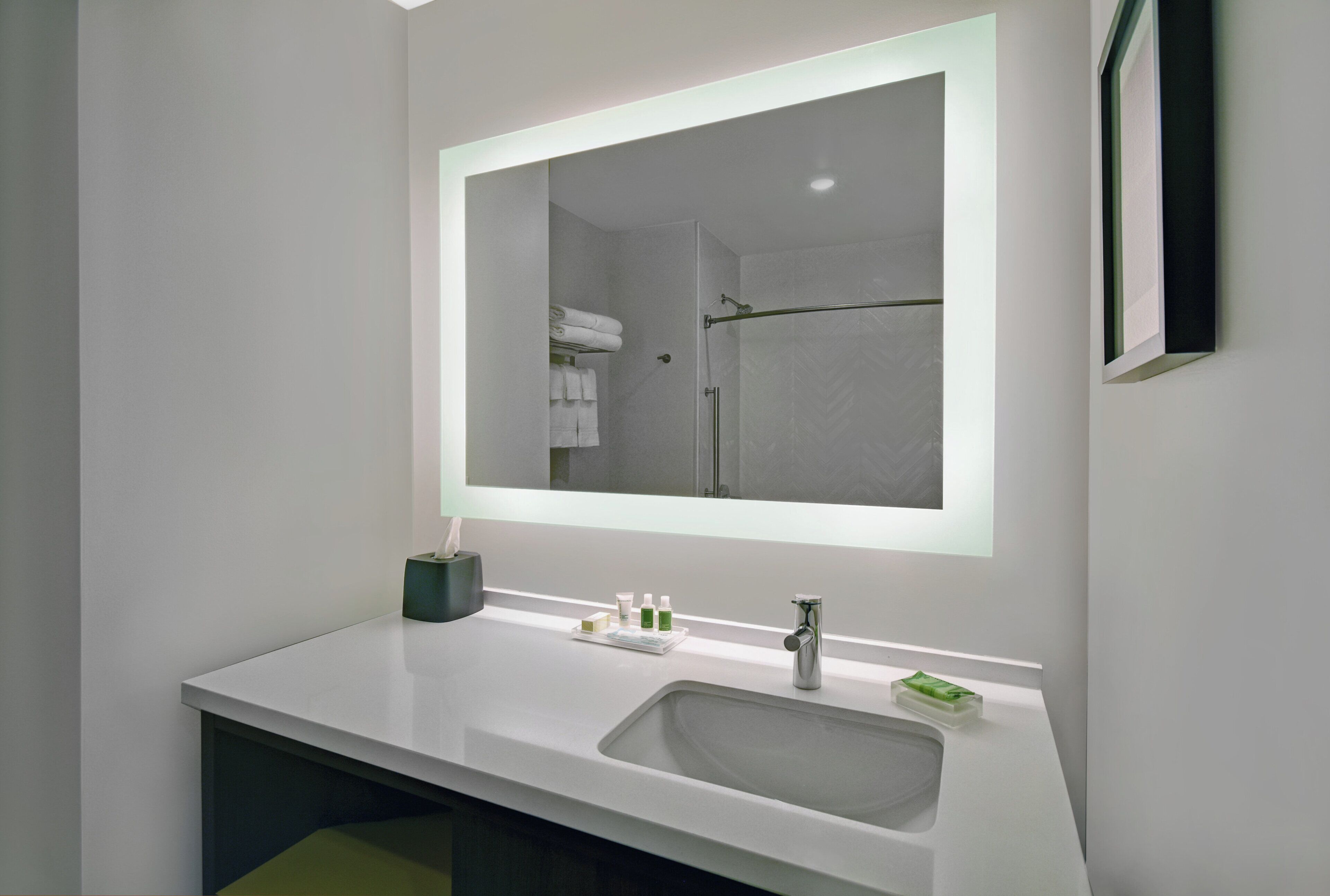 Une salle de bain moderne avec un grand miroir, un lavabo blanc et un porte-serviettes.
