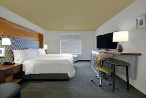 A hotel room with a bed, desk, chair, TV, lamp, and artwork on the wall. - Holiday Inn Grand Rapids North - Walker by IHG (Grand Rapids)