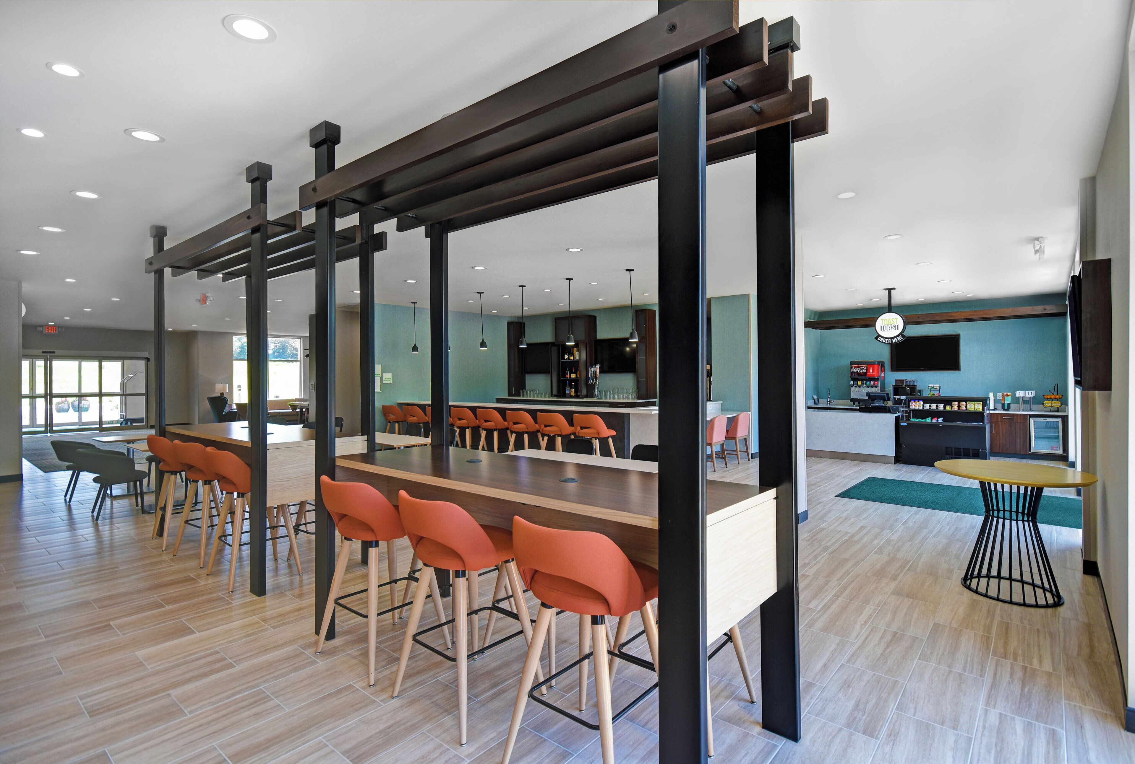 Un área de bar moderna con taburetes, una barra y un espacio de estar con mesas y sillas.