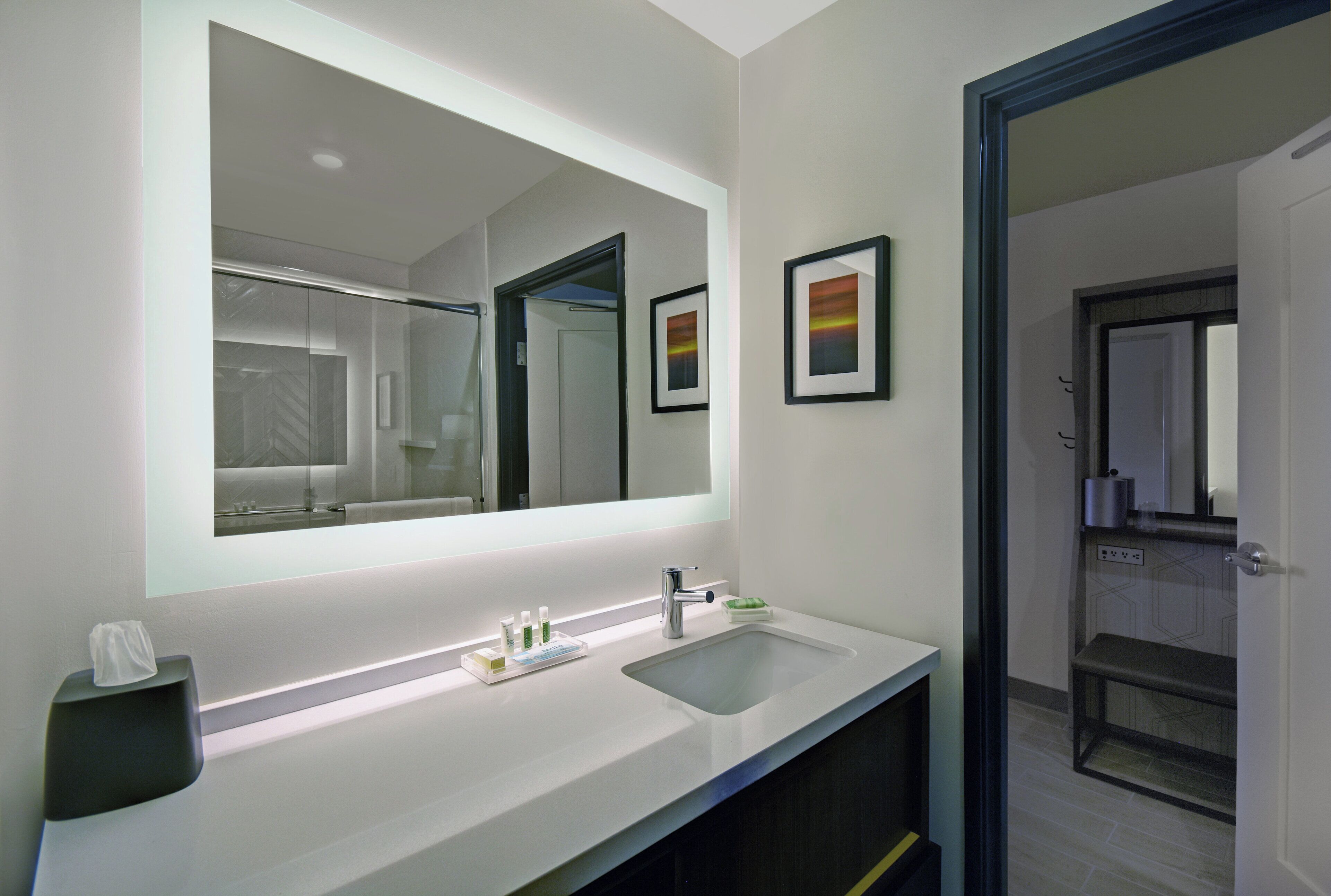 A modern bathroom with a large mirror, a sink, and a toilet. There are toiletries on the sink counter.