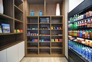 A kitchenette with a microwave, shelves stocked with snacks, and a refrigerator filled with beverages. - Holiday Inn Grand Rapids North - Walker by IHG (Grand Rapids)