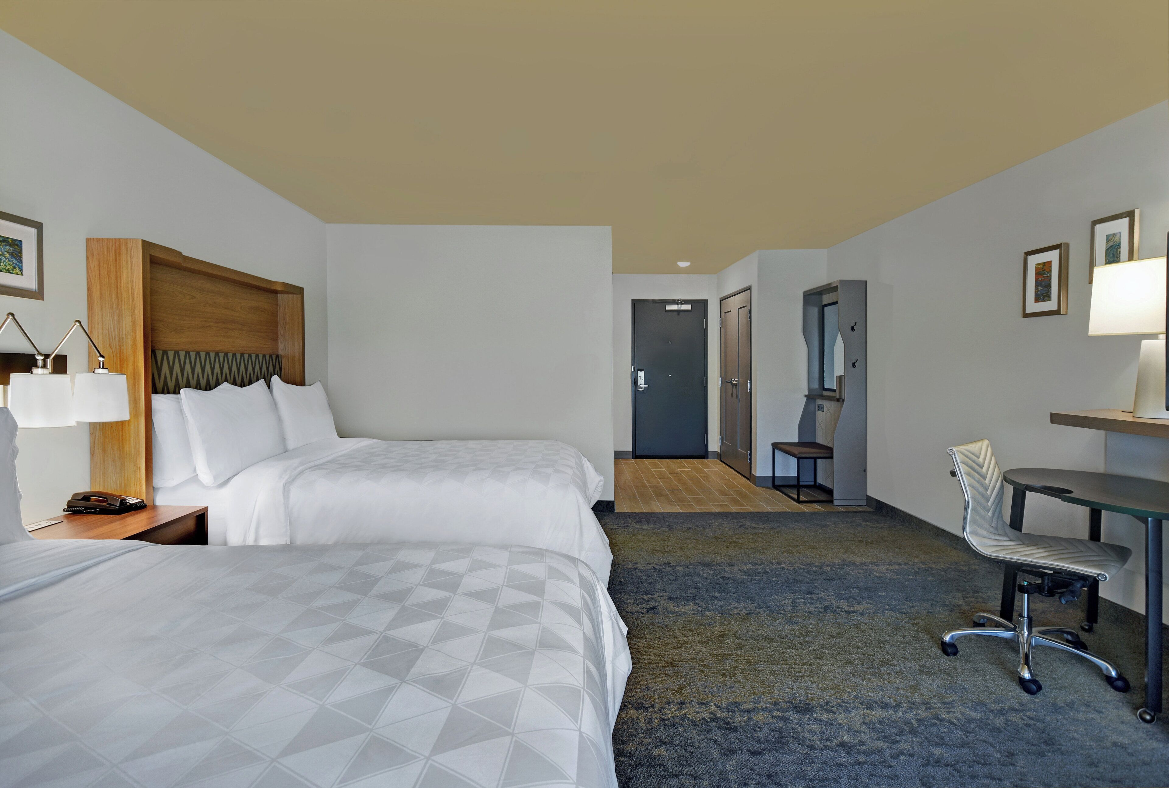 A hotel room with two beds, a desk, a chair, and a bathroom door.