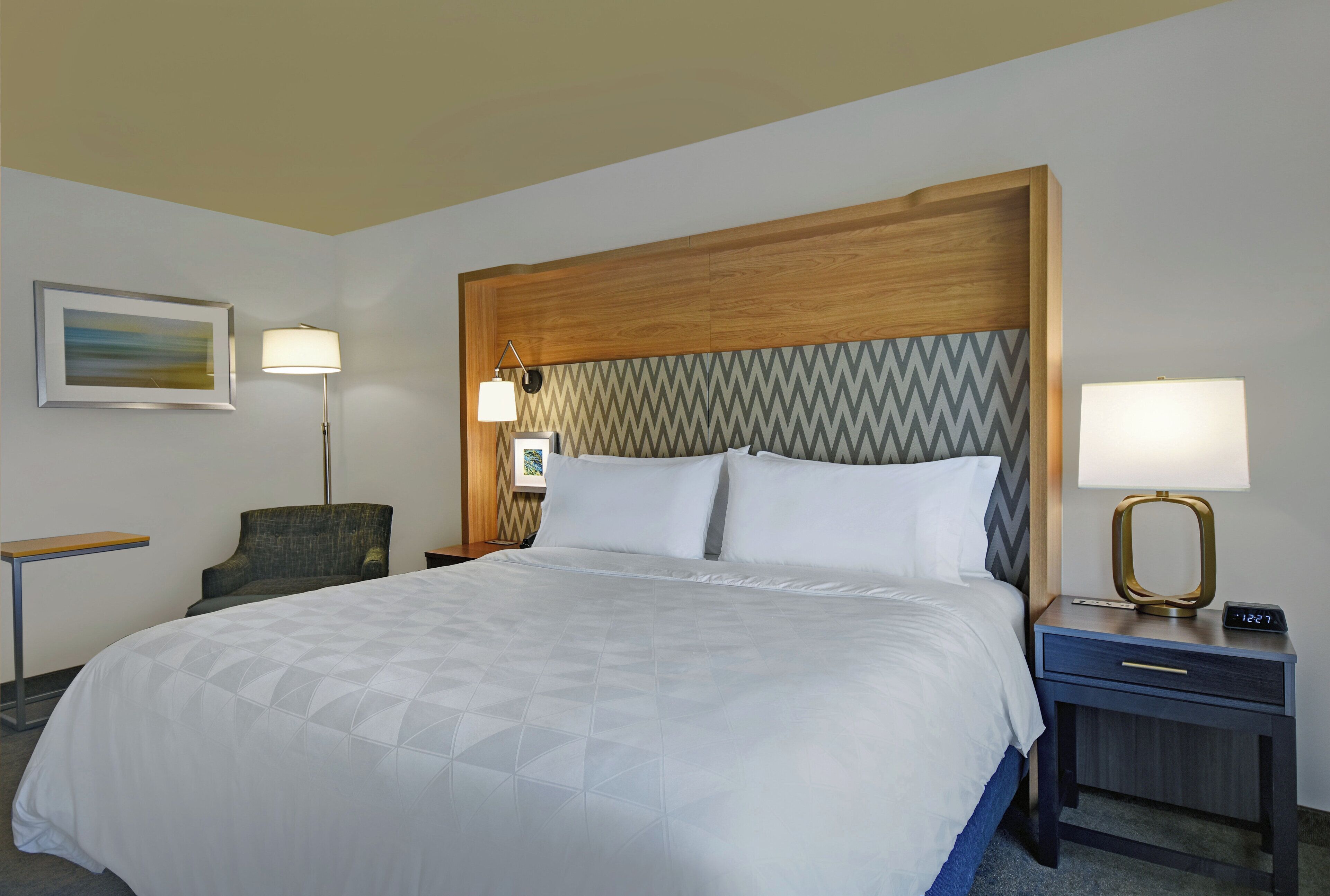 A hotel room with a bed, two bedside tables, a chair, a lamp, and a painting on the wall.