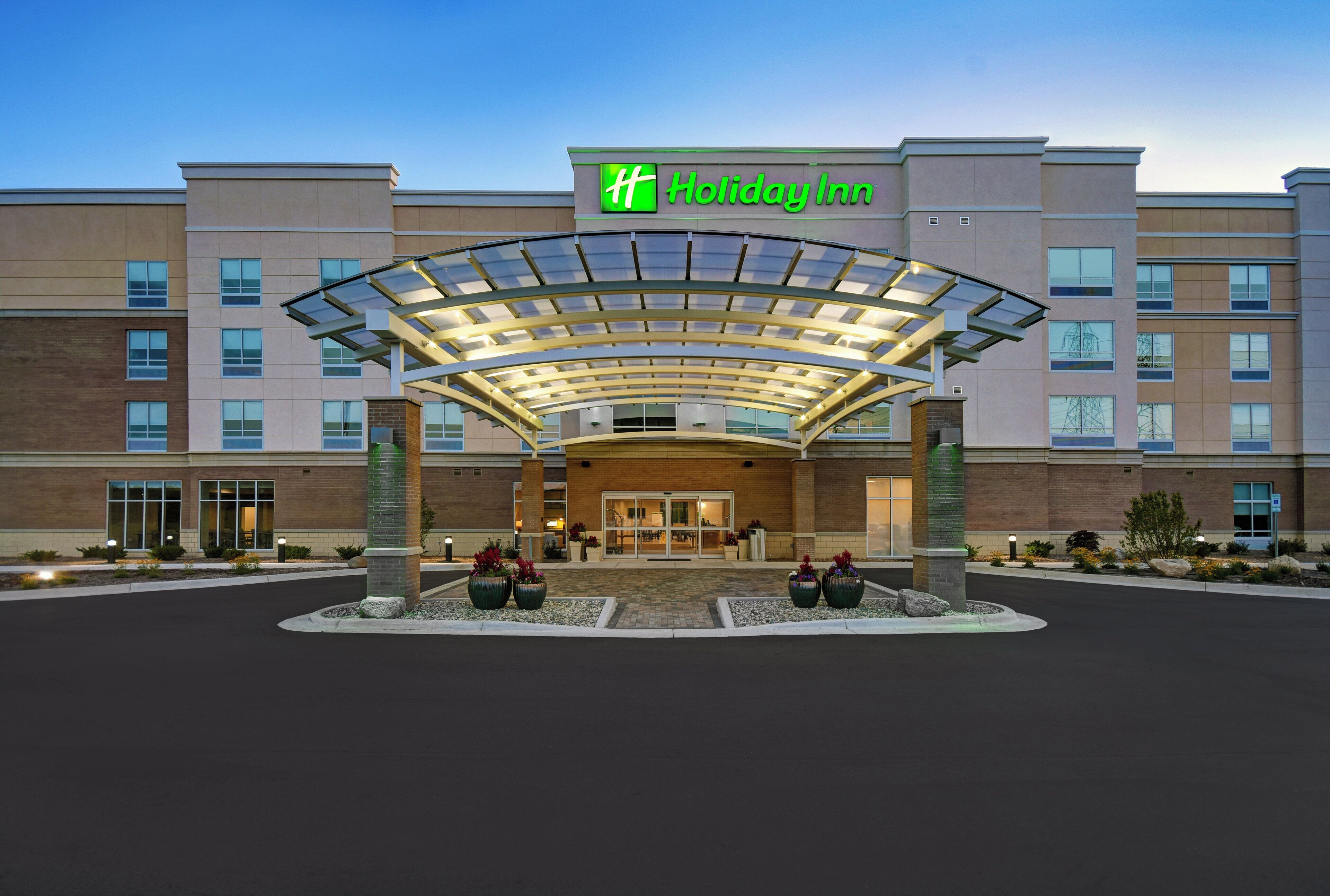A Holiday Inn hotel entrance with a covered walkway and large planters.
