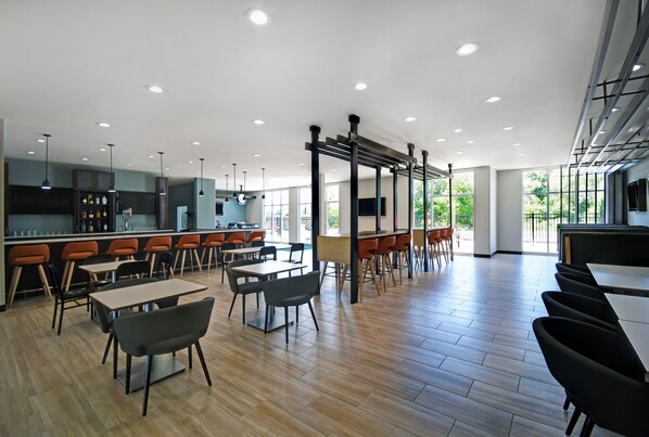 A modern restaurant with wooden flooring, black and orange chairs, and a bar area with stools. - Holiday Inn Grand Rapids North - Walker by IHG (Grand Rapids)