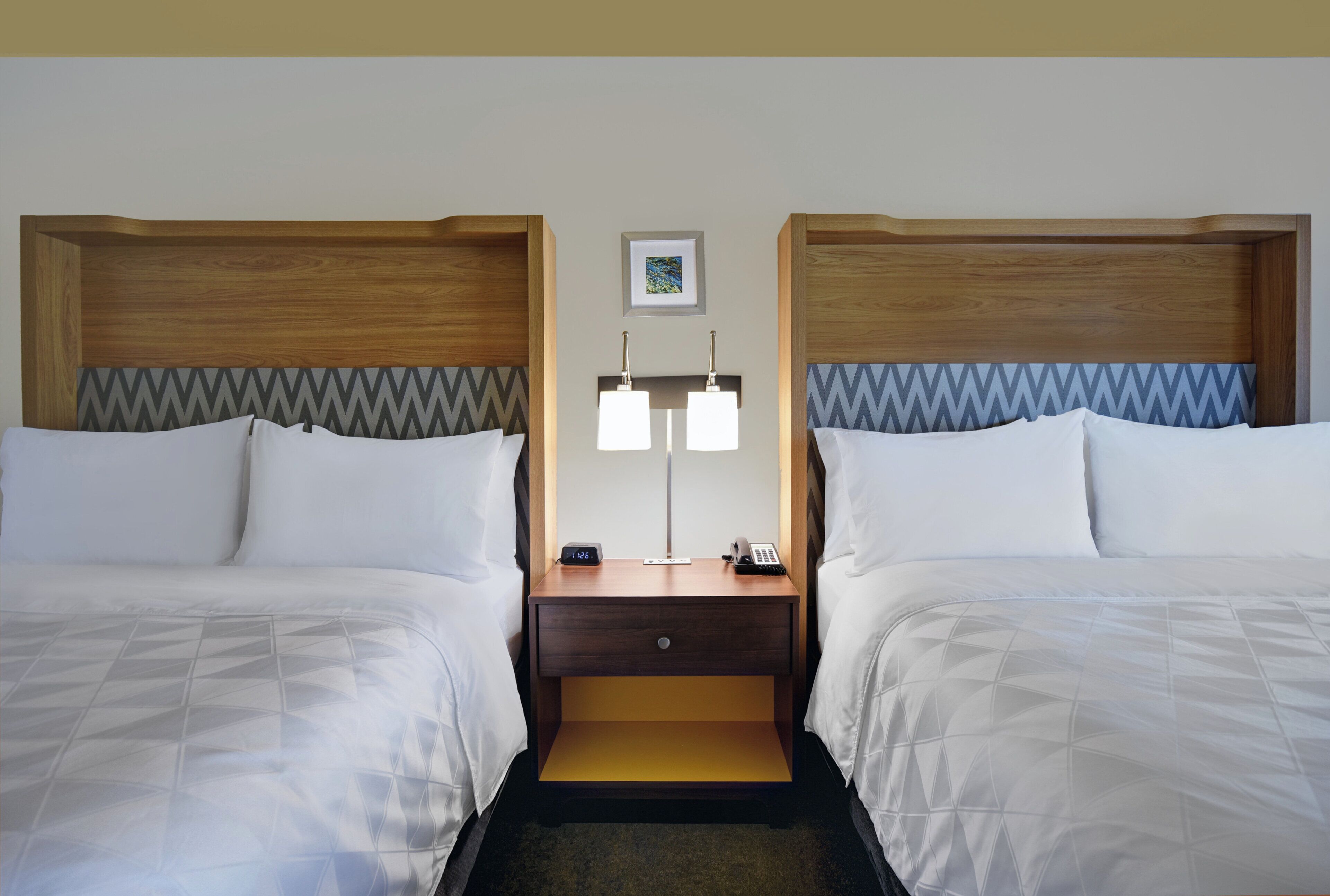 Een hotelkamer met twee bedden, een nachtkastje met een lamp, een klok en een telefoon.