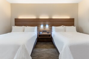 Quarto de hotel com duas camas, cabeceira de madeira, mesas de cabeceira com luminárias e uma pequena escrivaninha com telefone e controle remoto.