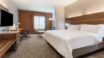 A hotel room with a large bed, a desk with a chair, a flat-screen TV, and a window.