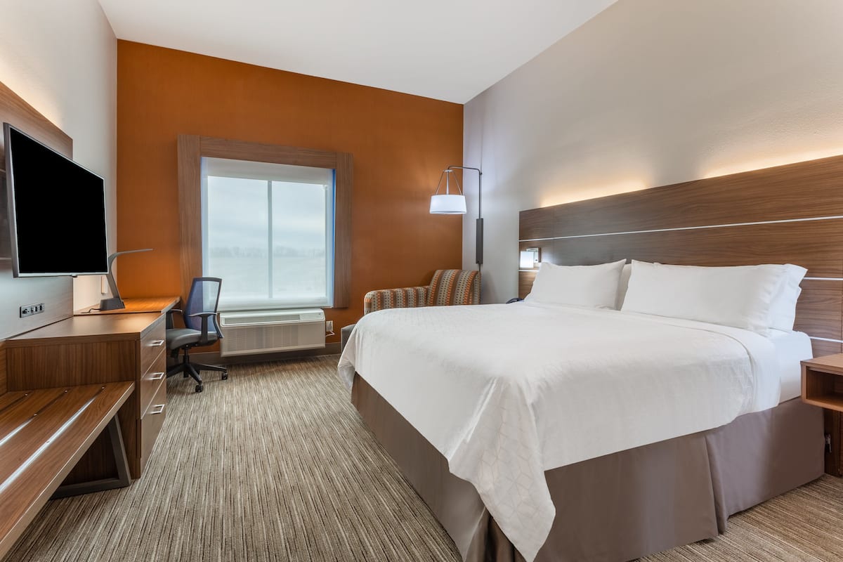 A hotel room with a large bed, a desk with a chair, a flat-screen TV, and a window with a view.