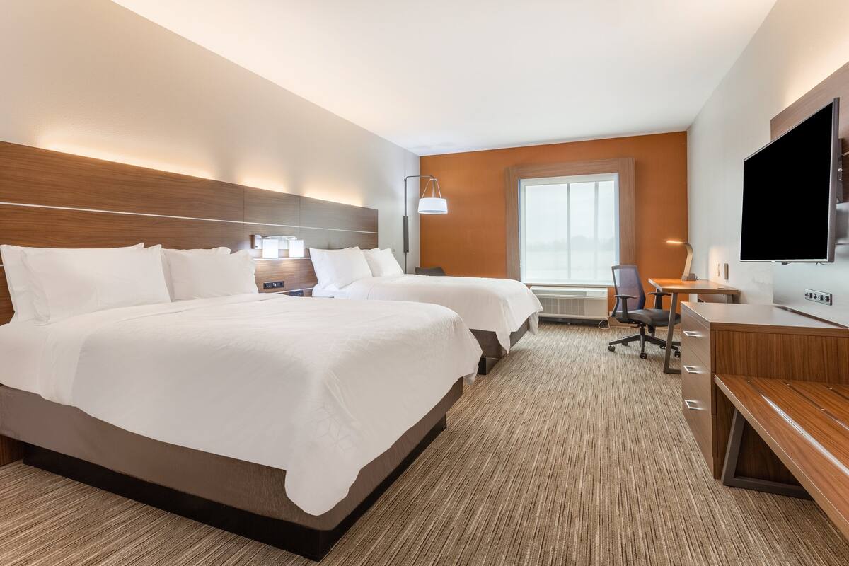 A hotel room with two beds, a desk, a chair, a TV, and a large window.