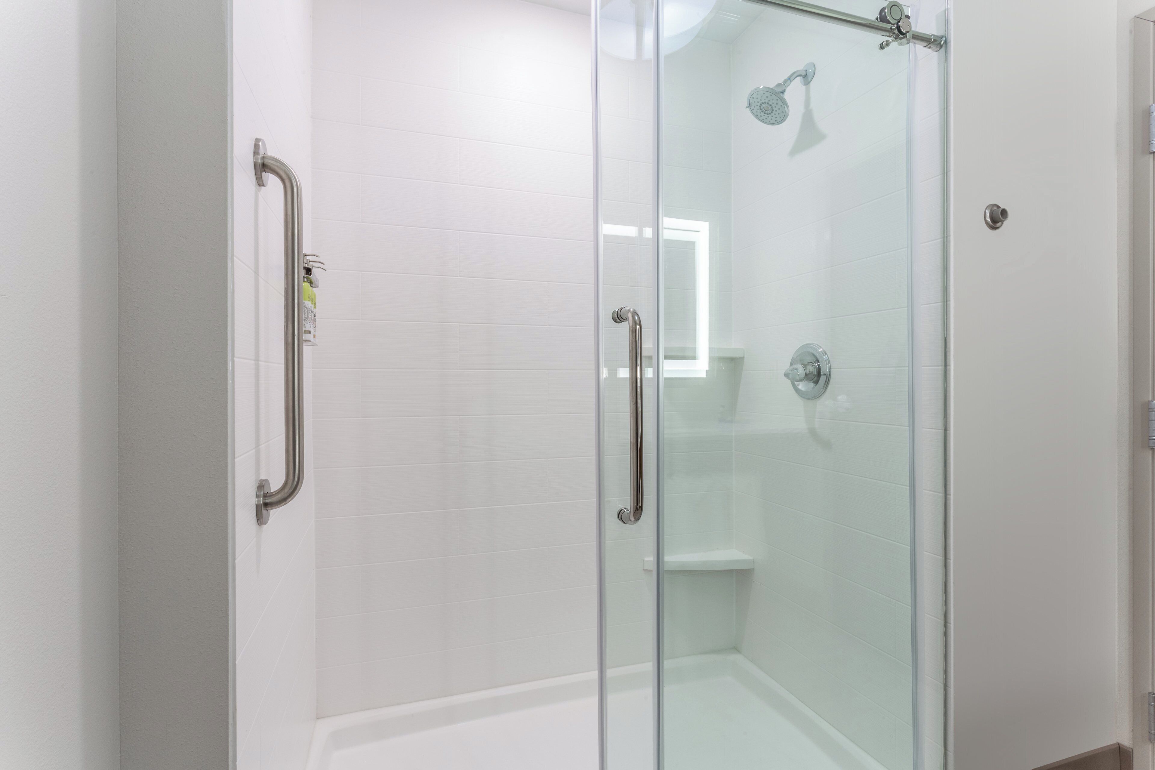 Een douchecabine met glazen wanden, een handdouche en een bediening voor de handdouche.