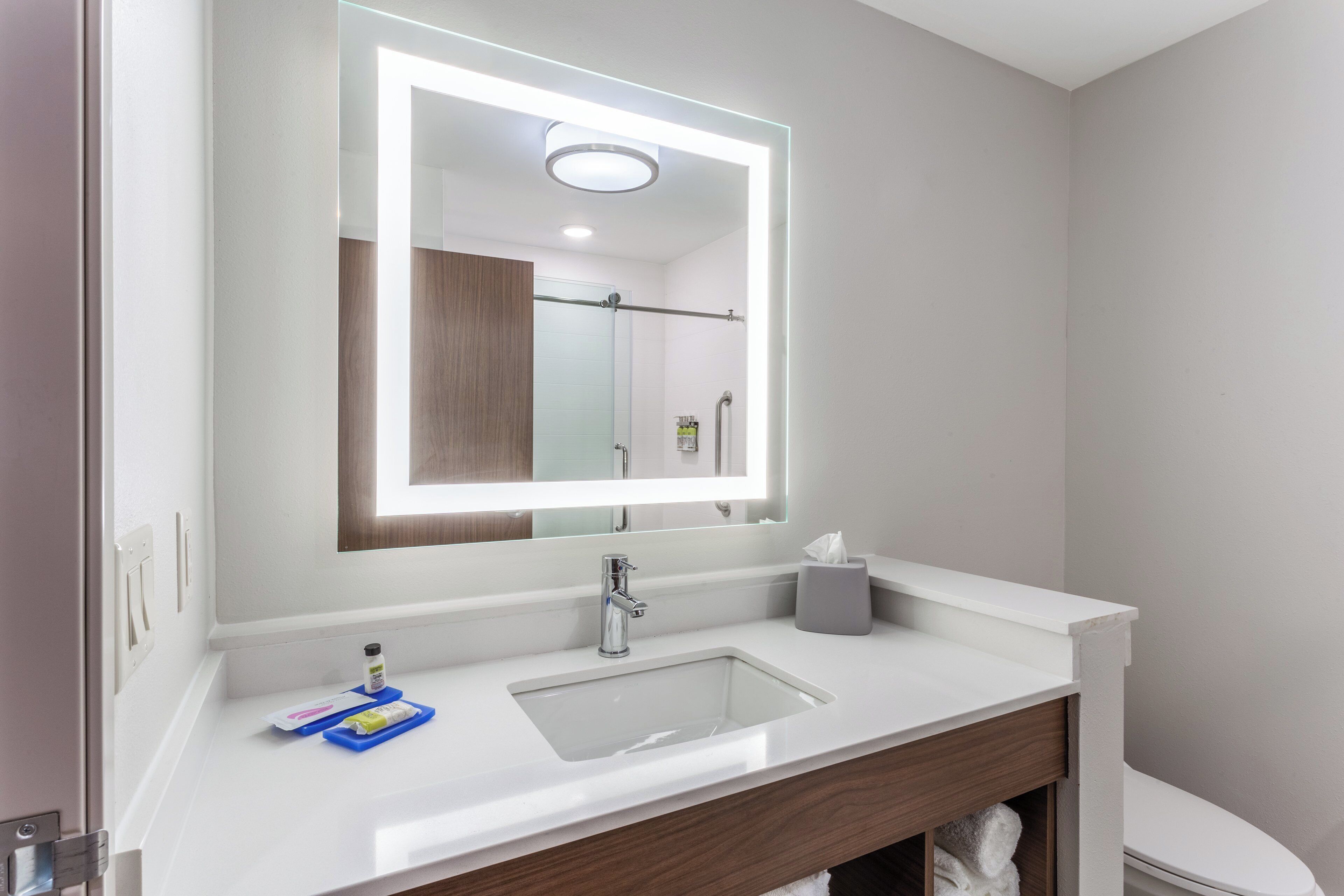 Un baño moderno con lavamanos blanco, un espejo con iluminación integrada, un perchero y un inodoro.