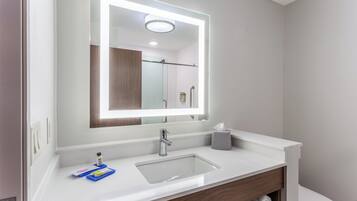 Un baño moderno con lavamanos blanco, un espejo con iluminación integrada, un perchero y un inodoro.