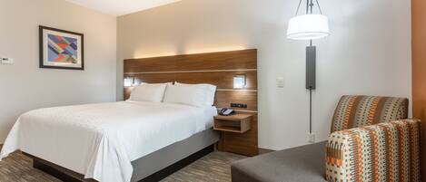 A hotel room with a bed, a nightstand, a lamp, and a patterned armchair.