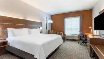 A hotel room with a large bed, a desk with a chair, a television, and a window with a view.