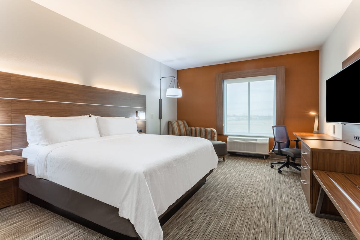 A hotel room with a large bed, a desk with a chair, a TV, and a window with a city view.