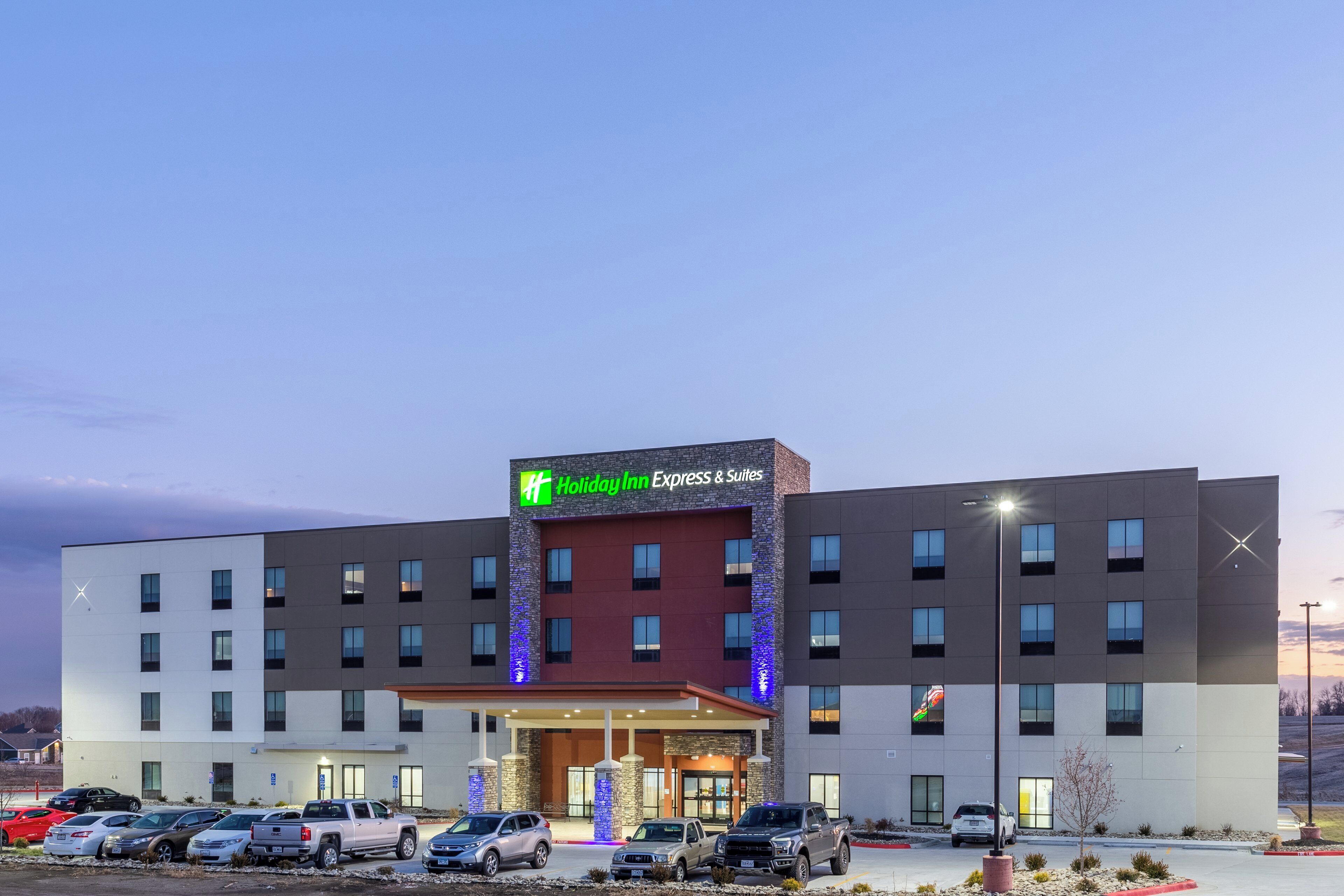 A Holiday Inn Express & Suites hotel with a modern design, featuring a prominent sign, multiple parking spaces, and a well-lit entrance.