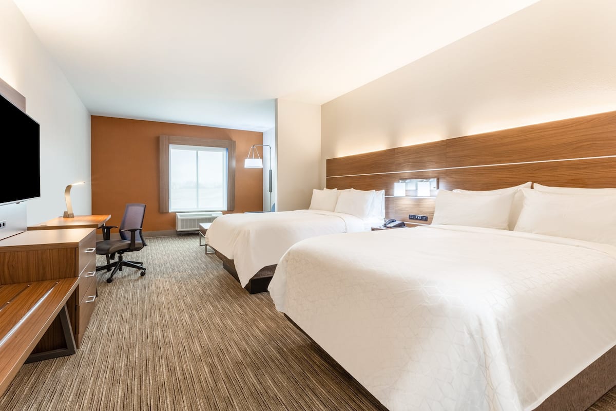 A hotel room with two beds, a desk with a chair, a flat-screen TV, and a large window.