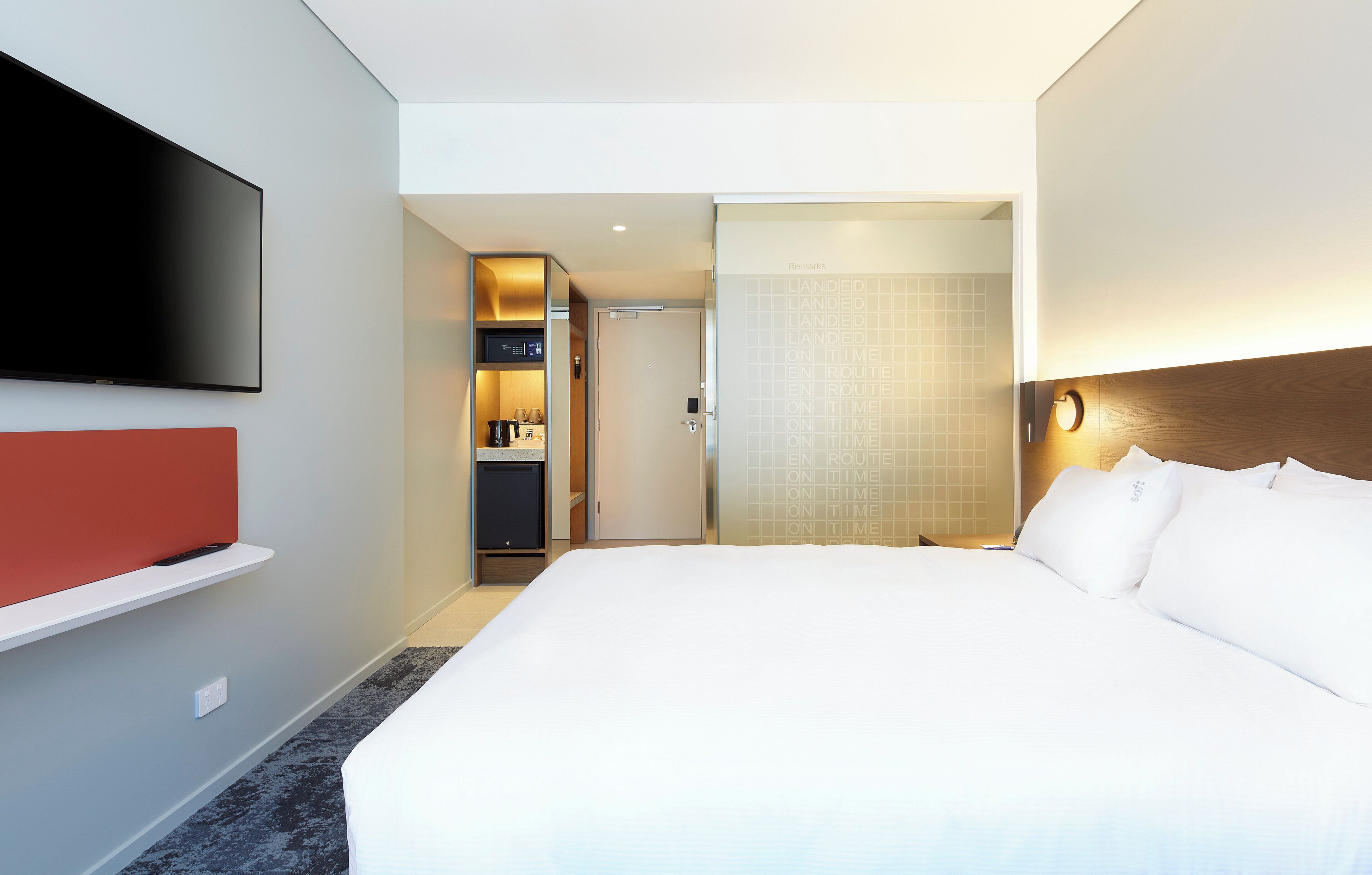 A hotel room with a large bed, a flat-screen TV mounted on the wall, a minibar, and a sliding door leading to a bathroom.