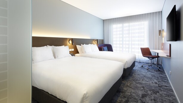A hotel room with two beds, a desk, a chair, and a TV mounted on the wall. - Holiday Inn Express Sydney Airport by IHG (Mascot)