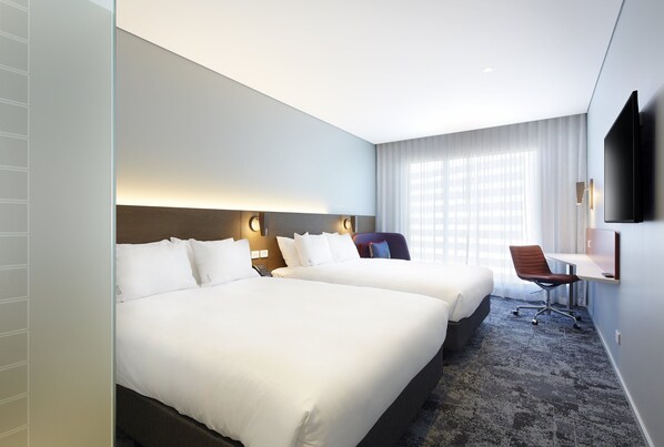Een hotelkamer met twee bedden, een bureau, een stoel en een aan de muur bevestigde televisie.