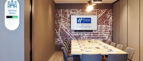 A meeting room with a large table, chairs, a screen displaying the Holiday Inn Express logo, and a sign indicating the room is vacant.