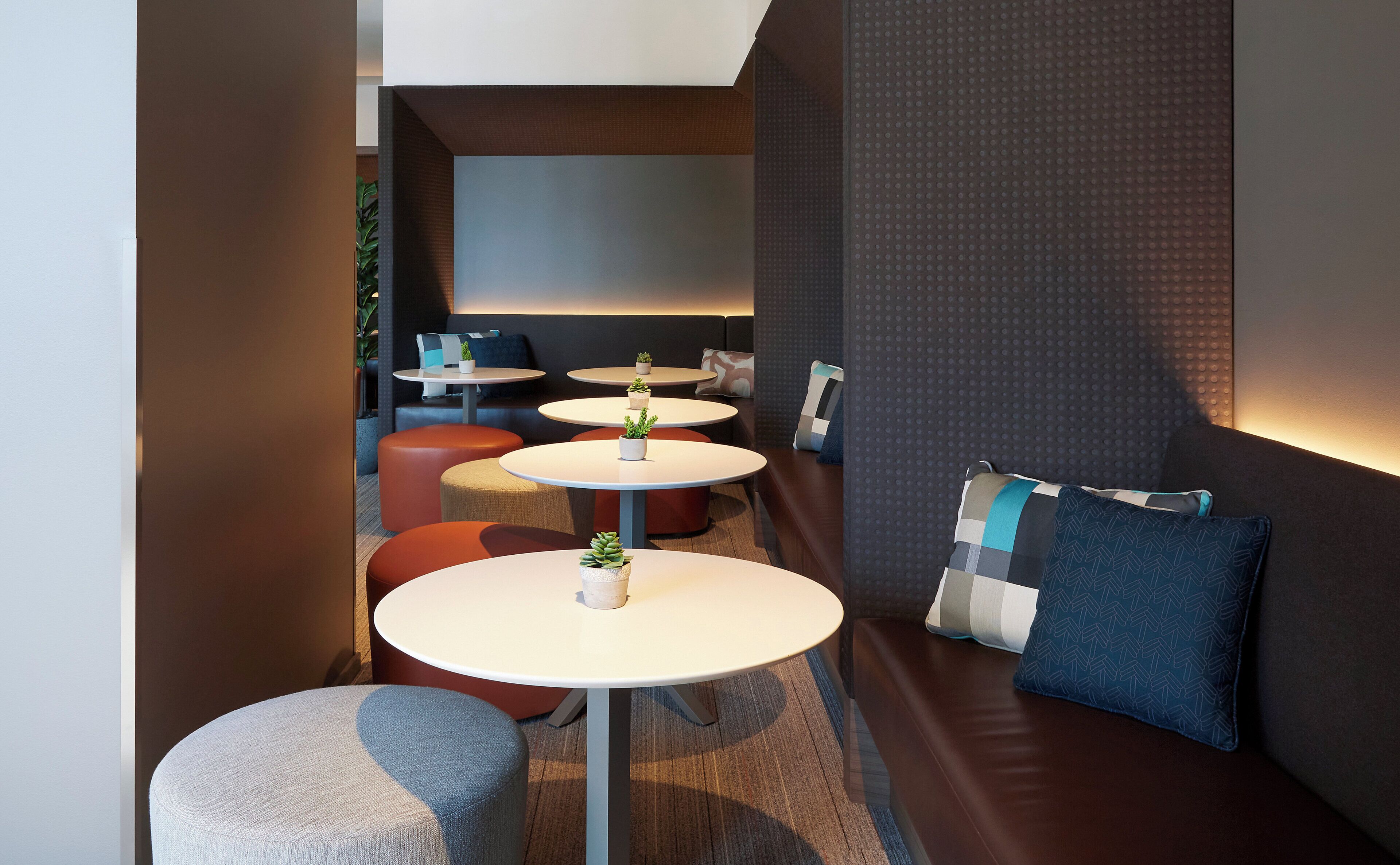 A modern lounge area with round tables, cushioned seating, and decorative pillows.