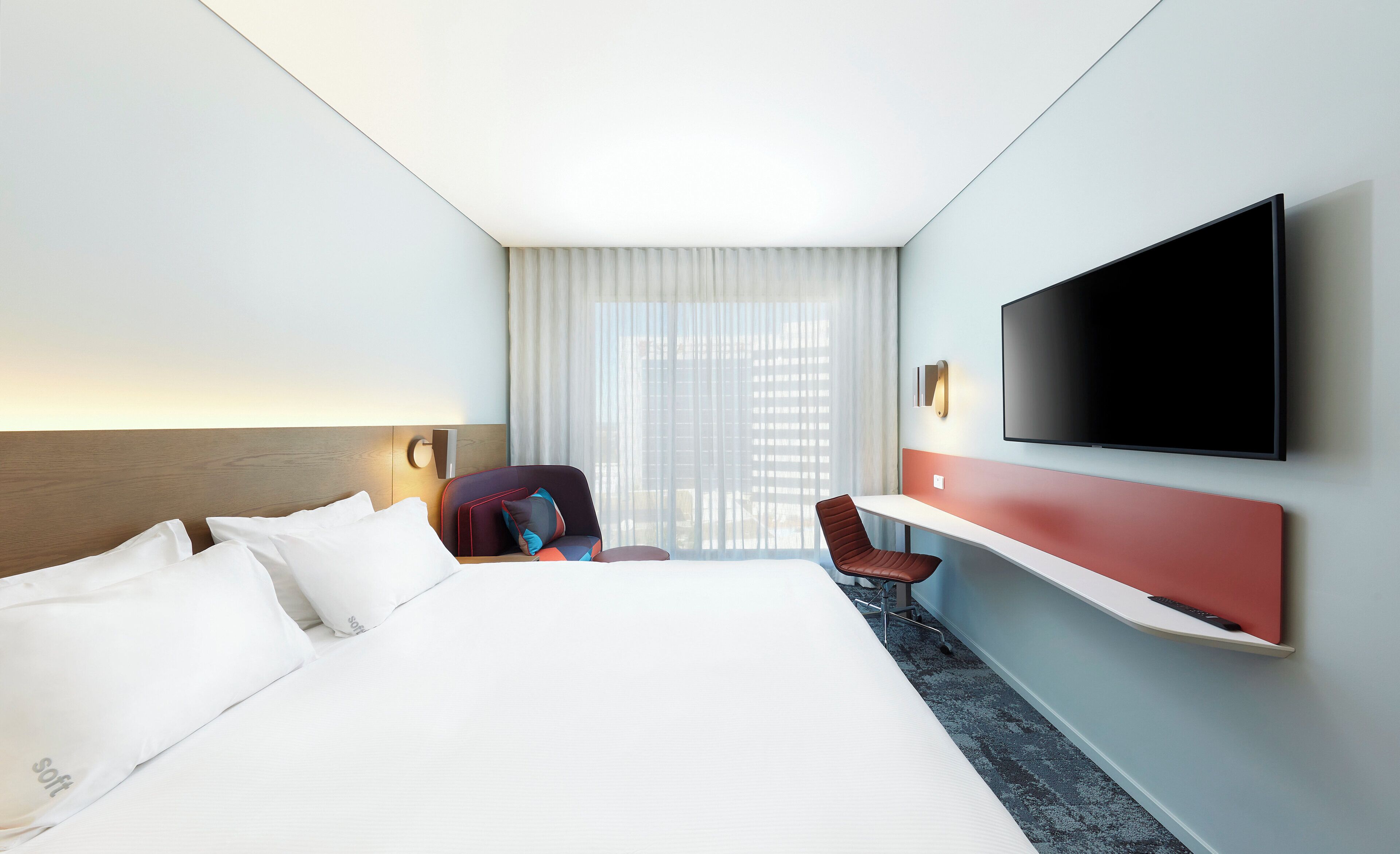 Habitación de hotel con cama, escritorio, silla, televisión y ventana con cortinas.