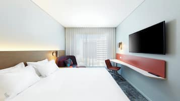 Habitación de hotel con cama, escritorio, silla, televisión y ventana con cortinas.