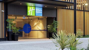 A Holiday Inn Express hotel entrance with a glass facade, security cameras, and potted plants.