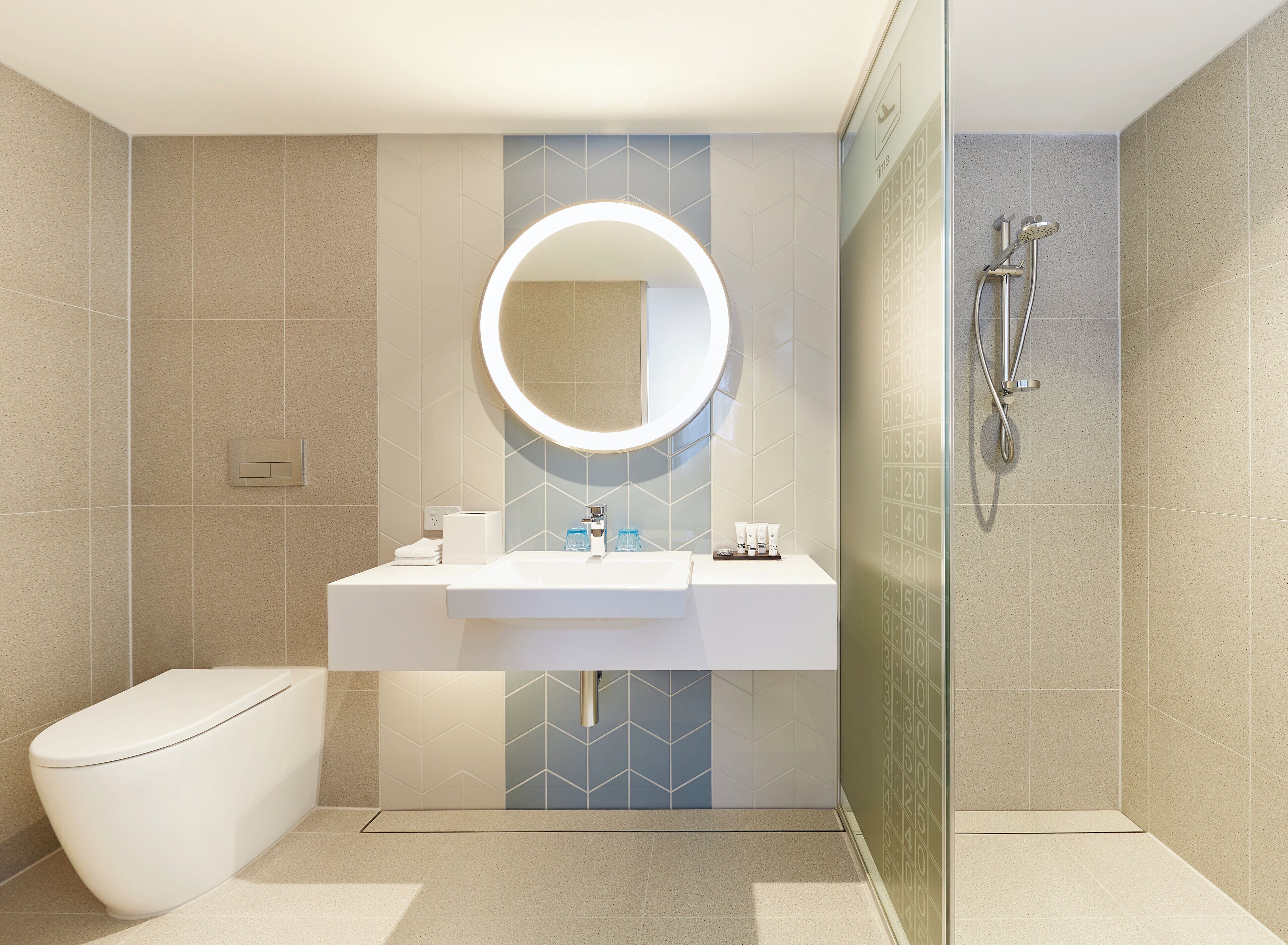 Un baño moderno con un lavamanos blanco, un espejo redondo, un inodoro y una zona de ducha.