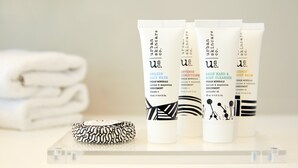 Three skincare products on a clear surface with a rolled towel and a patterned hairbrush in the background. - Holiday Inn Express Sydney Airport by IHG (Mascot)