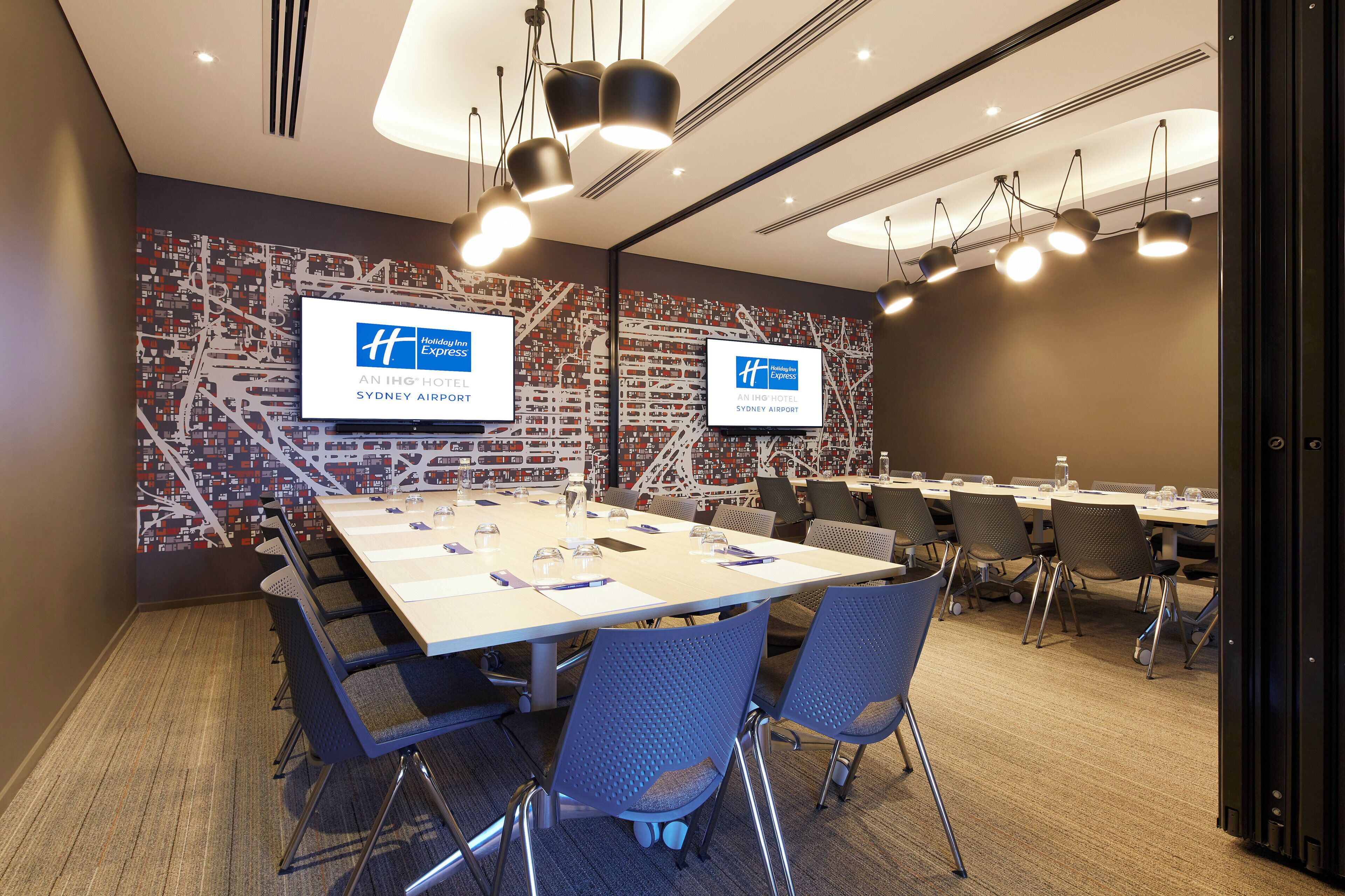 Un salón de conferencias con una larga mesa, sillas y dos pantallas que muestran el logotipo de Holiday Inn Express.