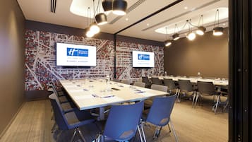 Un salón de conferencias con una larga mesa, sillas y dos pantallas que muestran el logotipo de Holiday Inn Express.