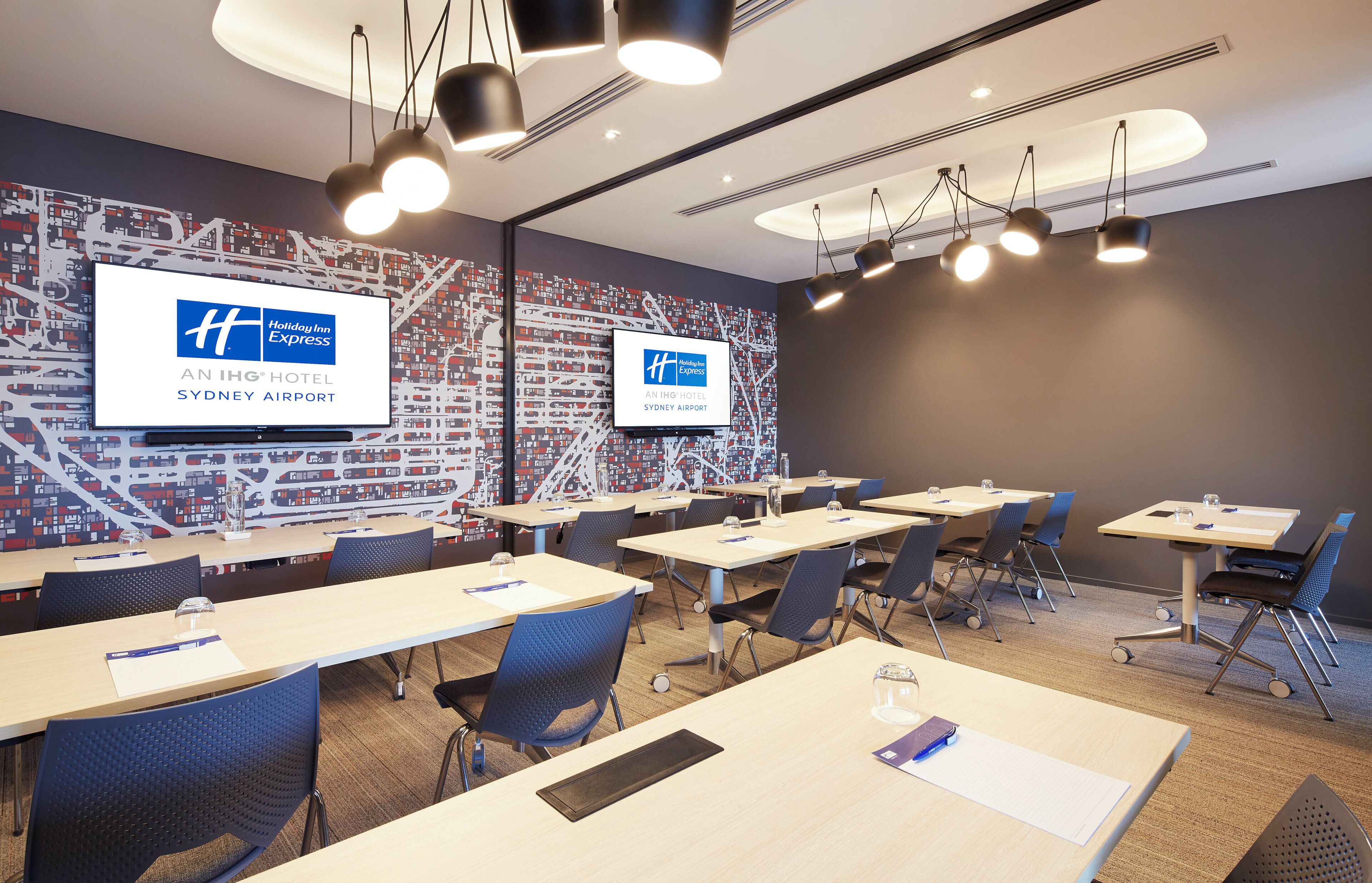 Un salón de conferencias con mesas, sillas y una pantalla grande mostrando el logotipo de Holiday Inn Express.
