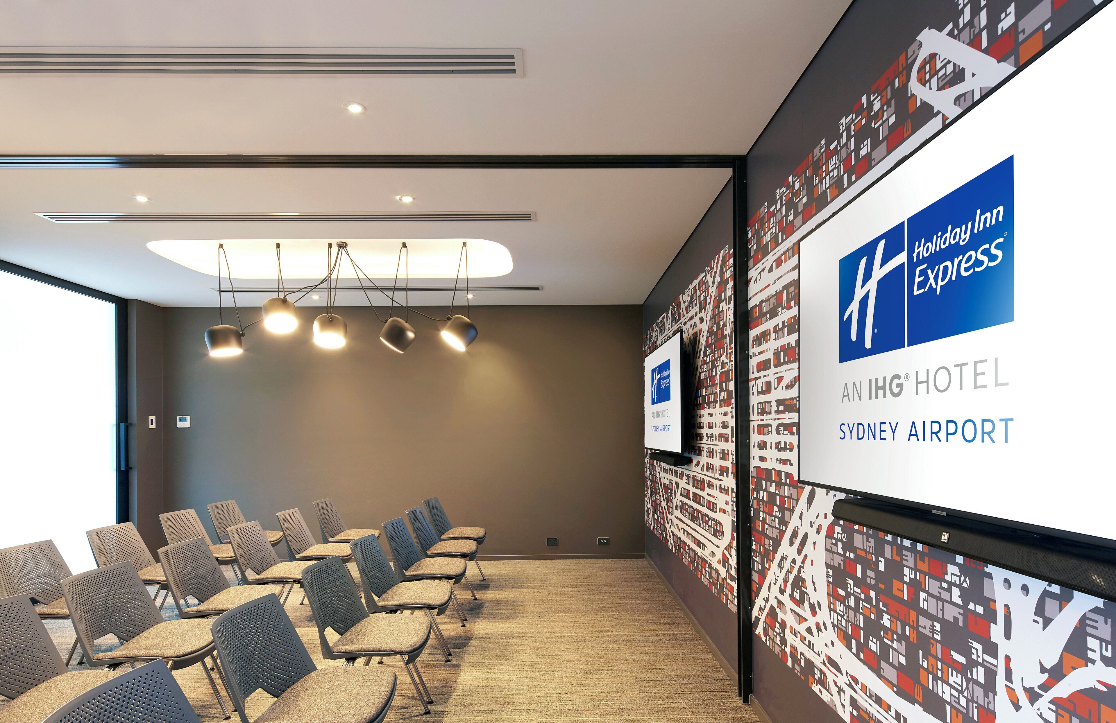 A conference room with rows of chairs, a ceiling light fixture, and a Holiday Inn Express sign on the wall.