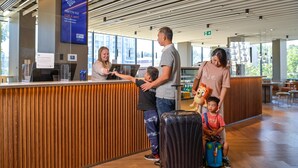 A reception area with a wooden reception desk, a digital screen displaying Wi-Fi information, and a view of the outdoors through large windows. - Holiday Inn Express Sydney Airport by IHG (Mascot)